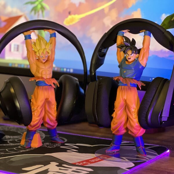 Two Goku Headphone Stands holding a set of gaming headsets. A Black haired Goku and a Super Saiyan to the left. Pictured on a stylish computer desk